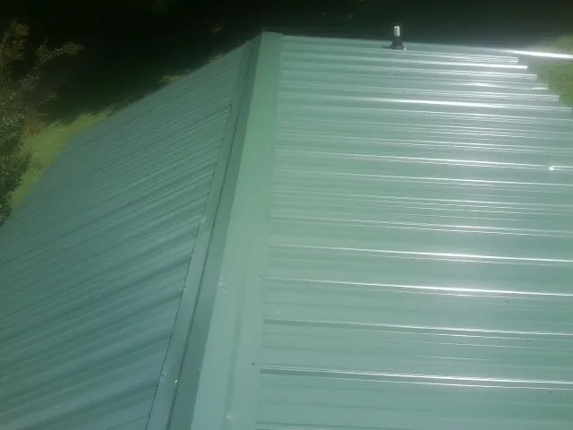 New green metal panels meeting at the ridge of a roof — Flat Roof Repair work by our crew in Little Rock