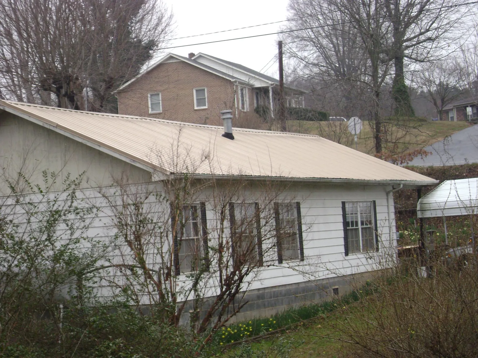 Tan metal roof on a white sided house set into a hillside — Commercial Roofing by Roofing Brothers in Little Rock